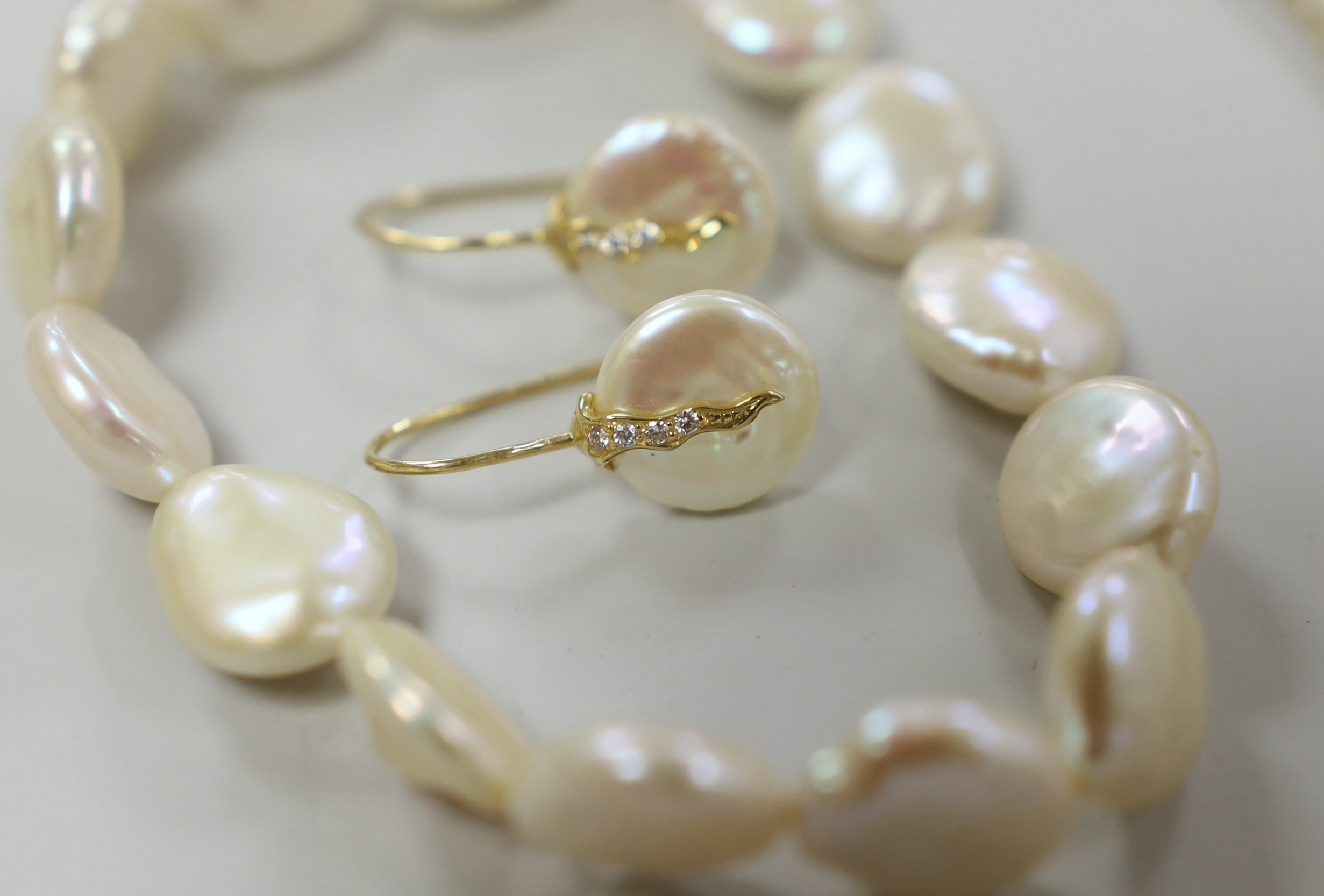 A modern suite of 750, diamond and button cultured pearl set jewellery, comprising a necklet and pair of earrings, together with a mother of pearl bracelet and a 375 necklet.